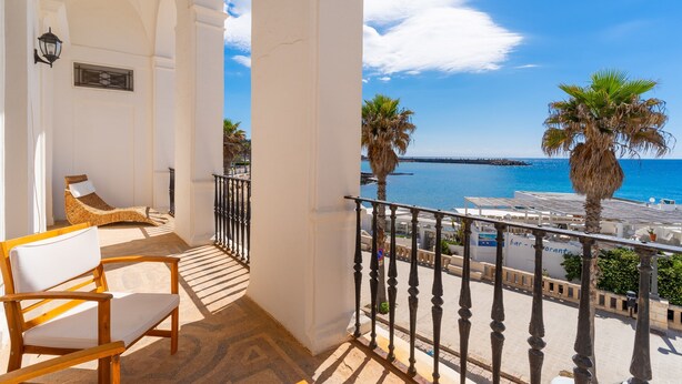 Varanda com vista para o mar, parede branca e cadeira de madeira.