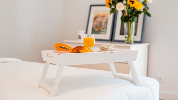 A breakfast tray with a glass of orange juice, a slice of papaya, and a croissant on a white bed. - Seaside Elegance and Tranquility (Porto)