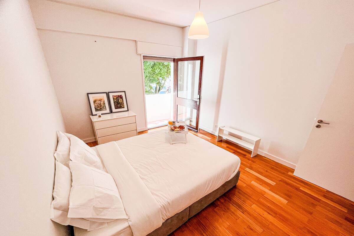 A bedroom with a bed, a bedside table with pictures, a bench, and a door.