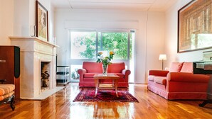 A living room with wooden flooring, a fireplace, two red sofas, and a vase with flowers on a coffee table. - Seaside Elegance and Tranquility (Porto)