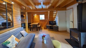 Et hyggeligt interiør i en træhytte med sofa, spisebord, fjernsyn og pejs.