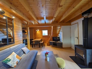 A cozy wooden cabin interior with a sofa, dining table, TV, and fireplace. - Chalet nordique au coeur de la Feclaz (La feclaz)