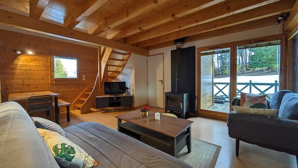 Et hyggeligt interiør i en hytte med træloft, sofa, fjernsyn og pejs.