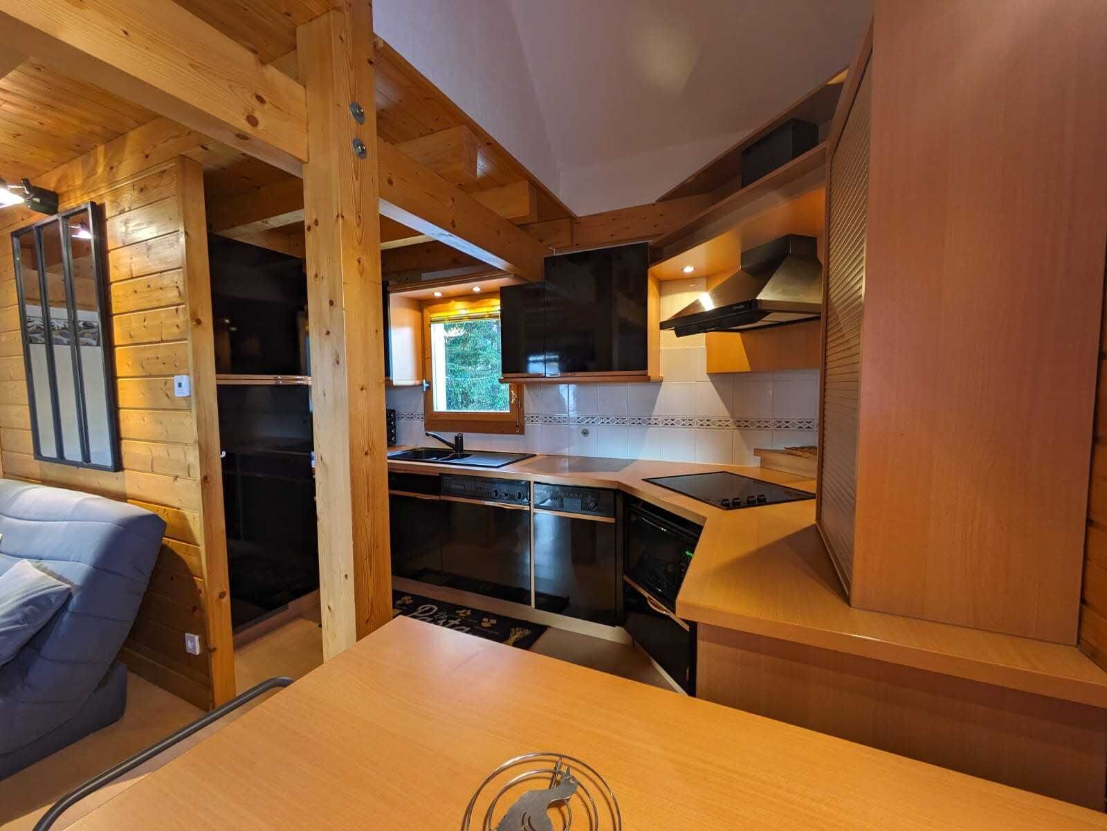 Une cuisine compacte avec des poutres en bois, une cuisinière intégrée et une fenêtre donnant sur un espace verdoyant.