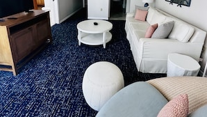 Uma sala de estar moderna com um sofá, um banquinho, uma mesa de centro e uma televisão de tela plana sobre um suporte de madeira.