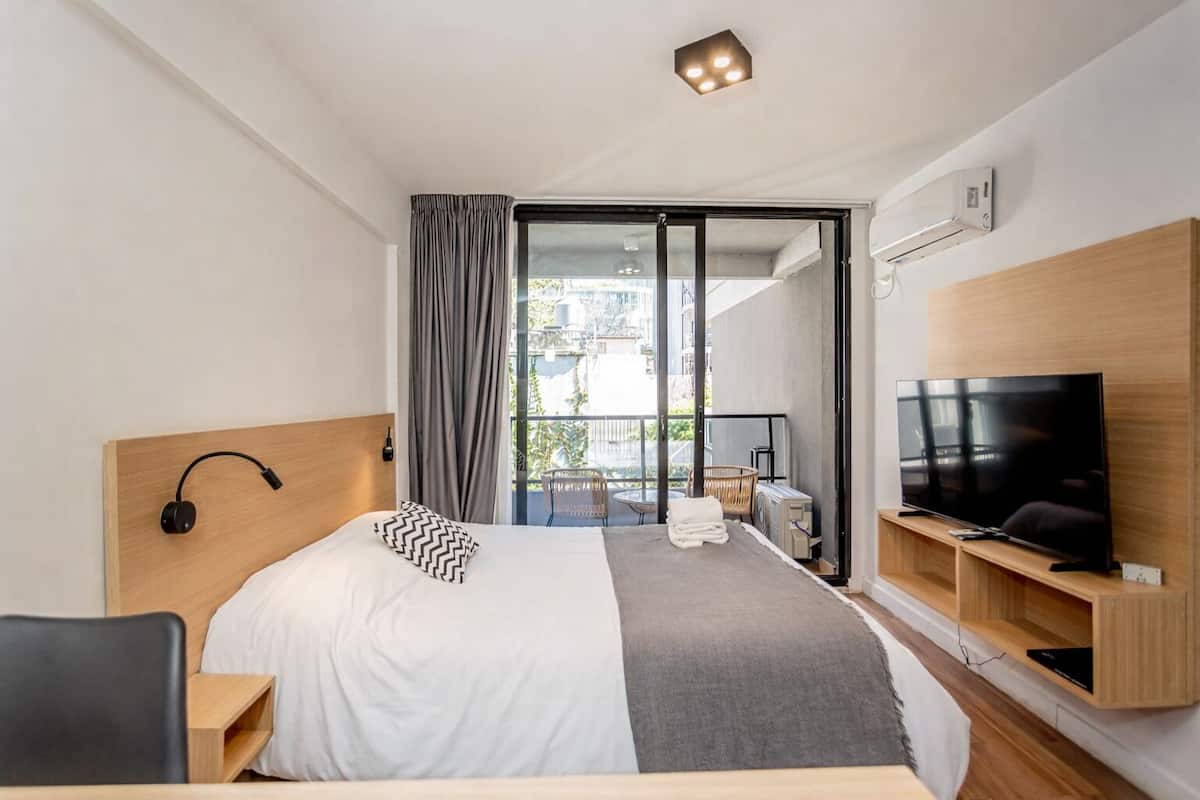 A hotel room with a bed, a TV, a desk, a chair, a balcony with a view, and a sliding door.