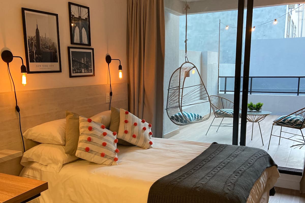 A modern bedroom with a large bed, a hanging chair, and a balcony with a table and chairs.