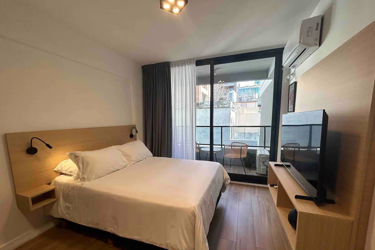A hotel room with a bed, a TV, a desk, and a balcony with a view.