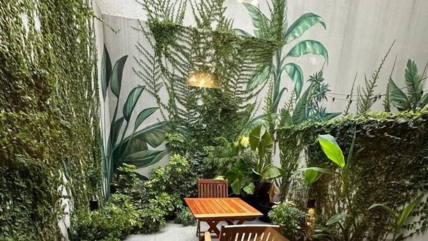 A patio area with a wooden table and chairs, surrounded by lush greenery and a wall mural. - Guatemala Studio 101 (Buenos Aires)
