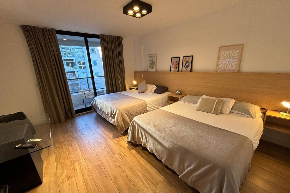 A hotel room with two beds, a desk, and a balcony with curtains.