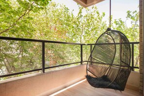Relax on the balcony with a hanging chair, taking in the serene views of lush greenery and trees.