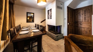 Un comedor con mesa de madera dispuesta para seis personas, chimenea y una puerta de madera grande.