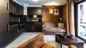 Un espacio habitable compacto con kitchenette, un sofá, una mesa y un ventanal con cortinas.