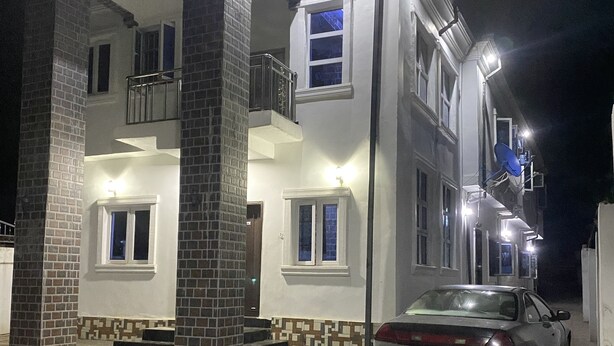 A two-story building with a balcony on the second floor, a car parked in front, and a satellite dish on the roof. - Divine Villa and Resorts LTD (Umu Ezeukwu)