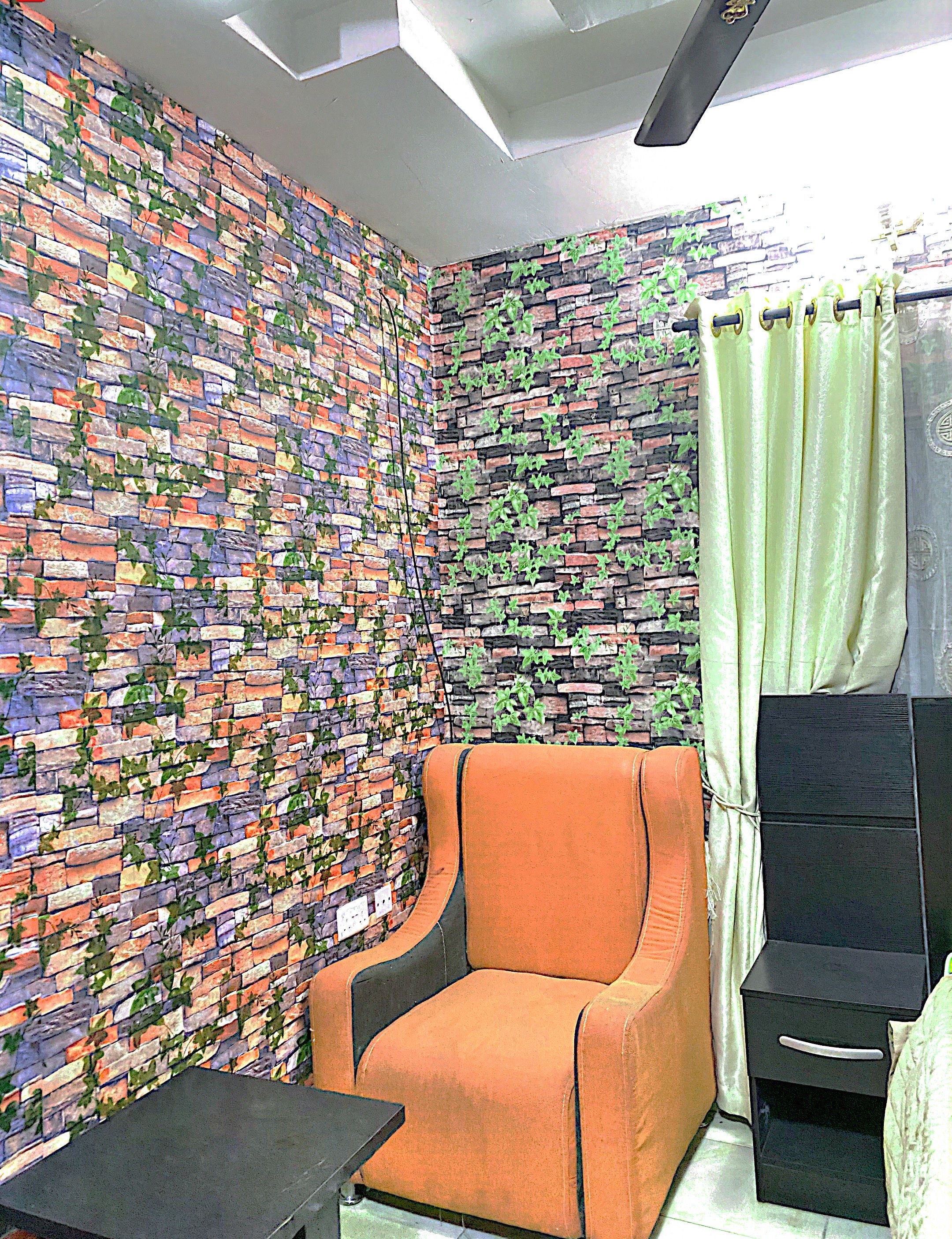 Una habitación con pared de ladrillo, un sillón naranja, una mesita de noche negra y una cortina verde.