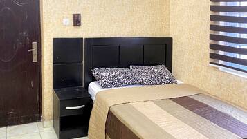 A bedroom with a bed, a nightstand, a ceiling fan, a window with blinds, and a door.