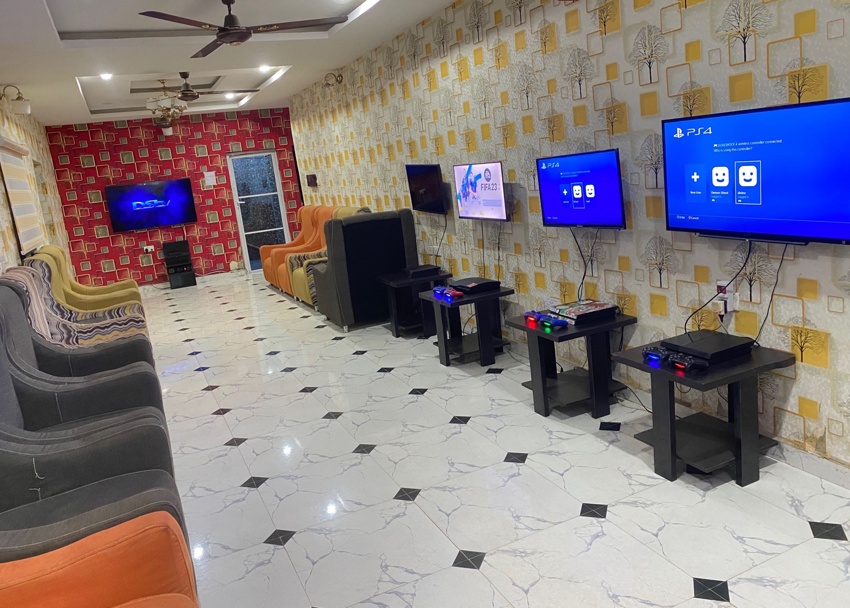 A gaming lounge with multiple gaming stations, a large screen TV, and a patterned wall.