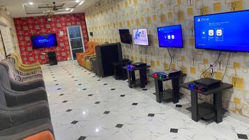 A gaming lounge with multiple gaming stations, a large screen TV, and a patterned wall.