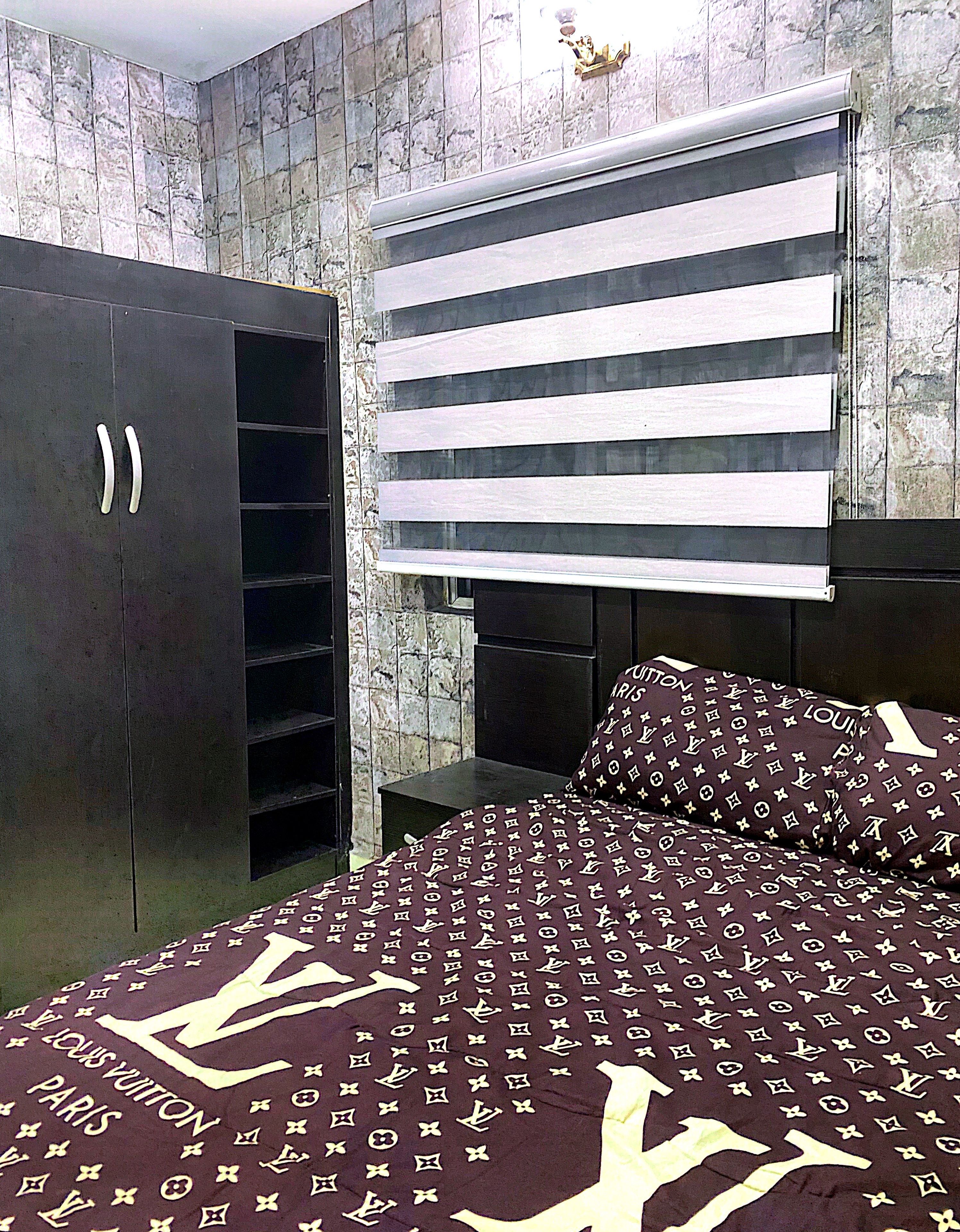 Un dormitorio con un armario, una cama con edredón estampado y una ventana con persianas horizontales.
