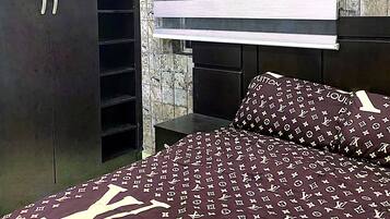 Un dormitorio con un armario, una cama con edredón estampado y una ventana con persianas horizontales.