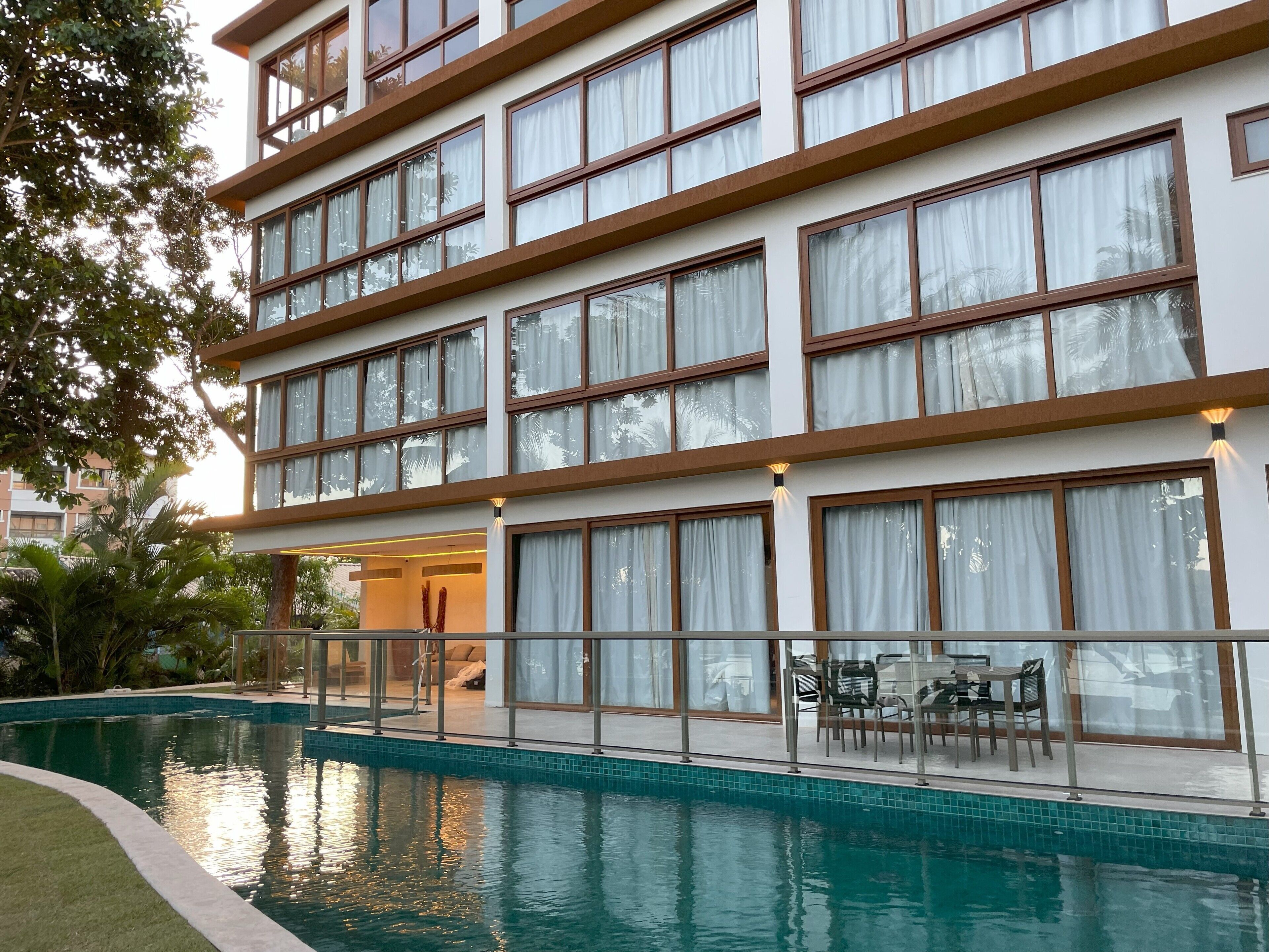 A multi-story hotel with a swimming pool, outdoor seating, and large windows.