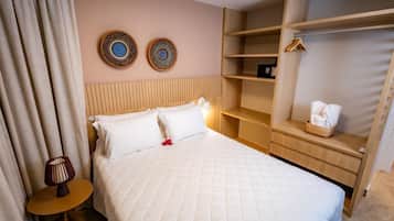 Habitación de hotel con cama, mesita de noche con lámpara, cabecero de madera, armario y dos adornos en la pared.