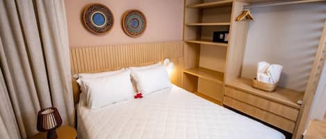 Ein Hotelzimmer mit Bett, Nachttisch mit Lampe, Holz Kopfteil, Kleiderschrank und zwei Wandbildern.