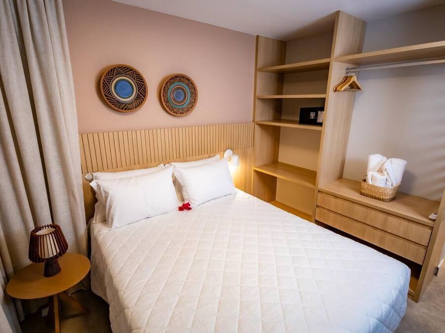 Habitación de hotel con cama, mesita de noche con lámpara, cabecero de madera, armario y dos adornos en la pared.