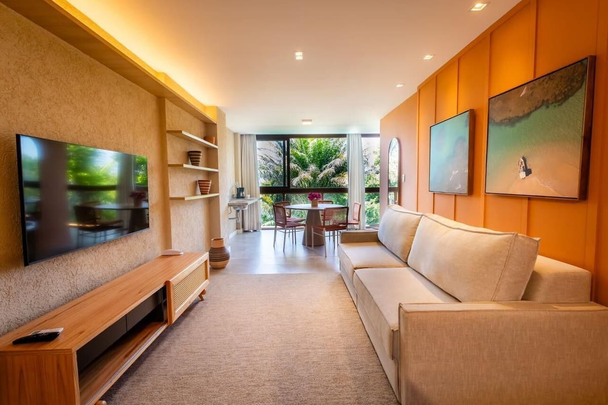 Un salon moderne doté d’un téléviseur à écran plat, d’un meuble de rangement en bois, d’un canapé beige et d’un coin repas avec une table et des chaises.