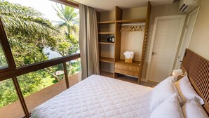 Une chambre avec un grand lit, une armoire, un miroir et une vue sur la verdure environnante.