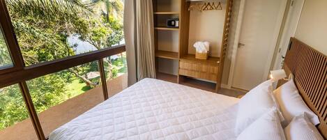 A bedroom with a large bed, a wardrobe, a mirror, and a view of greenery outside.