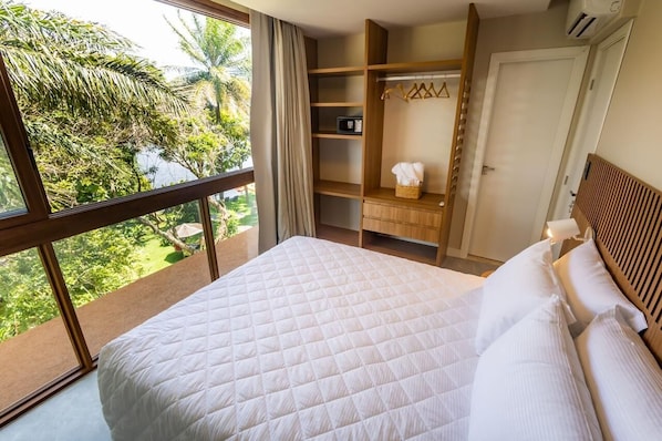 A bedroom with a large bed, a wardrobe, a mirror, and a view of greenery outside. - Guarajuba Suites Premium Boutique Hotel (Camaçari)