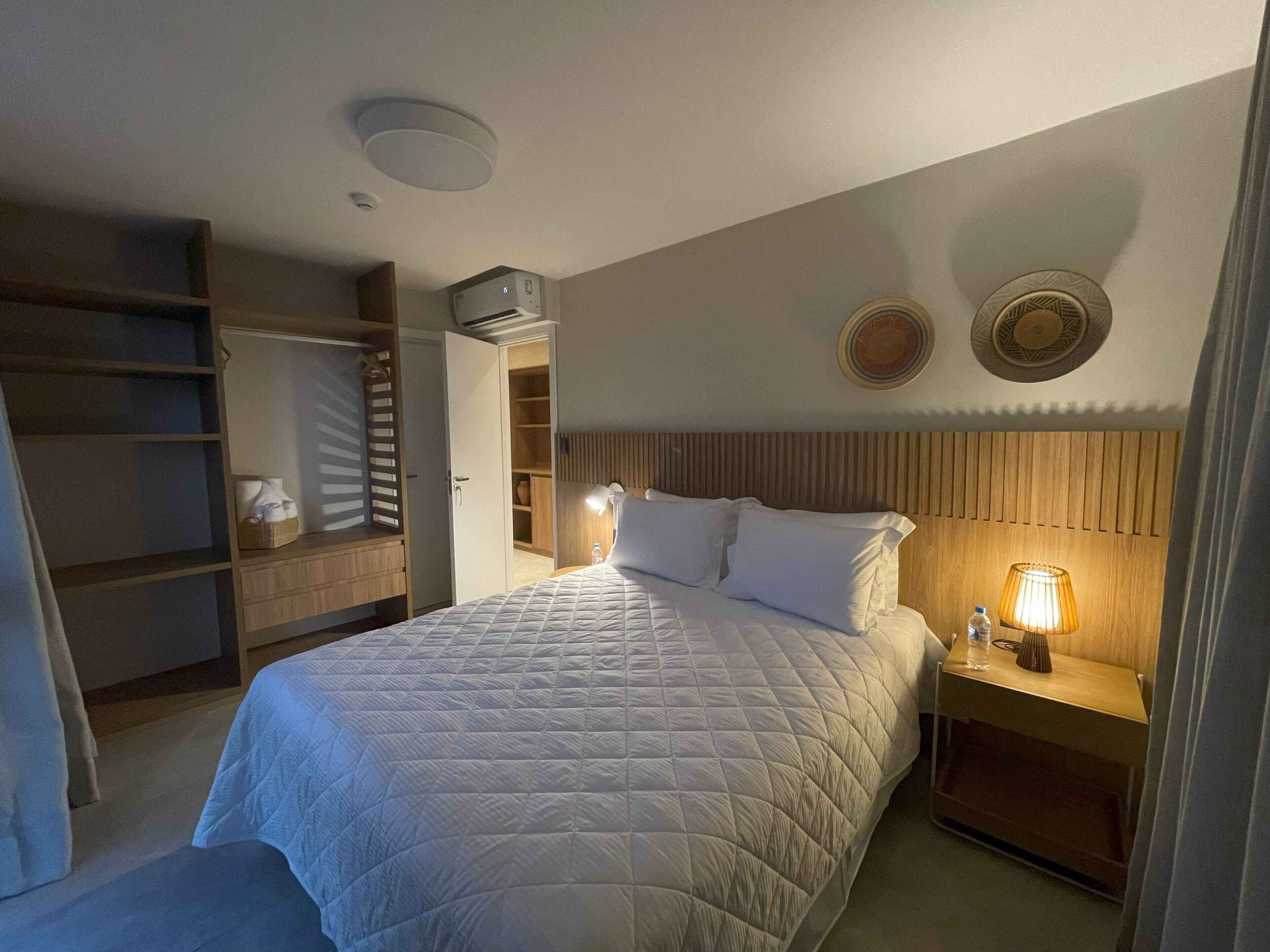 Een keurig opgemaakt slaapkamer met een bed, nachtkastje, lamp en een garderobe.