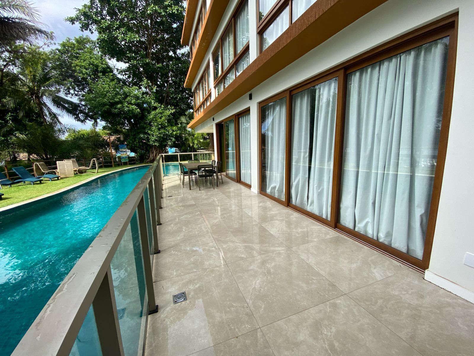 Zona junto a la piscina con vista despejada, una mesa de comedor con sillas y un edificio con amplios ventanales.