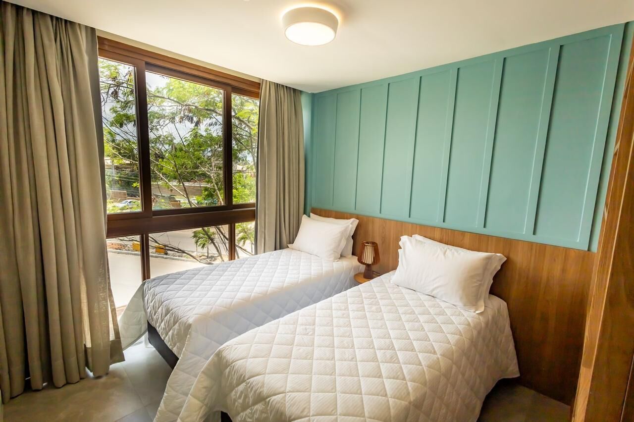 Habitación de hotel con dos camas, una ventana con cortinas, una pared de acento color verde azulado e iluminación en el techo.