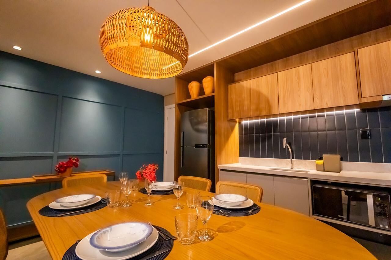 A modern dining area with a wooden table set for four, a large woven pendant light, and a kitchen with dark tiles and wooden cabinets.