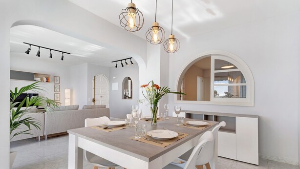 Een moderne eetruimte met een houten tafel voor vier personen, witte stoelen en hanglampen.