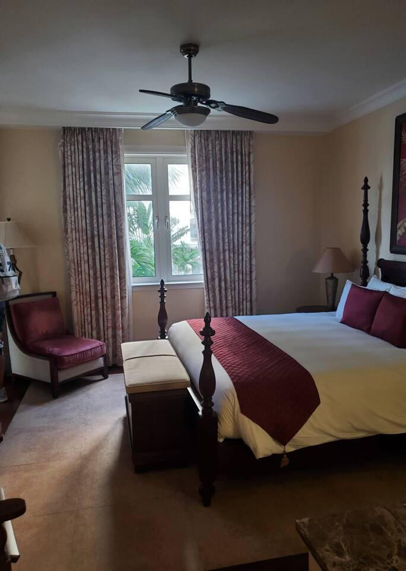 Ein Schlafzimmer mit einem Himmelbett, einem Sessel, einem Nachttisch und einem Deckenventilator.