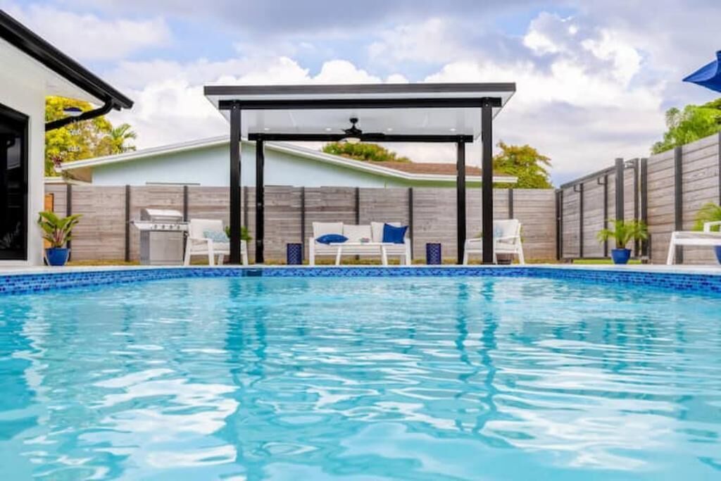 Una piscina con sillones de descanso y una pérgola.
