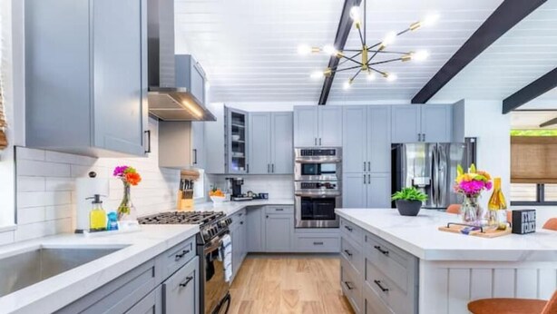 Une cuisine moderne avec des meubles gris, un îlot central, des appareils en acier inoxydable et un plancher en bois.