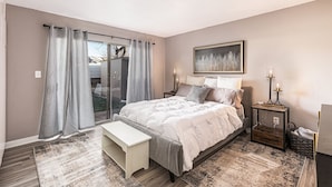 Une chambre à coucher comprenant un lit, des tables de chevet, un banc, une petite table avec une lampe et un tableau au mur.