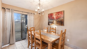 Un coin repas avec une table et des chaises en bois, un lustre, un tableau et une porte-fenêtre coulissante.