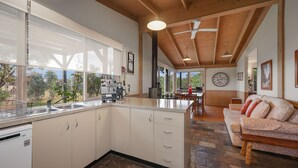A modern kitchen with a large island, wooden ceiling beams, and a view of the outdoors. - Wollondilly - Mansfield - Sleeps 10 (Goughs Bay)