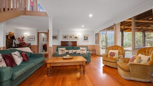 A spacious living room with a wooden floor, a green sofa set, a beige armchair, and a wooden coffee table. - Wollondilly - Mansfield - Sleeps 10 (Goughs Bay)