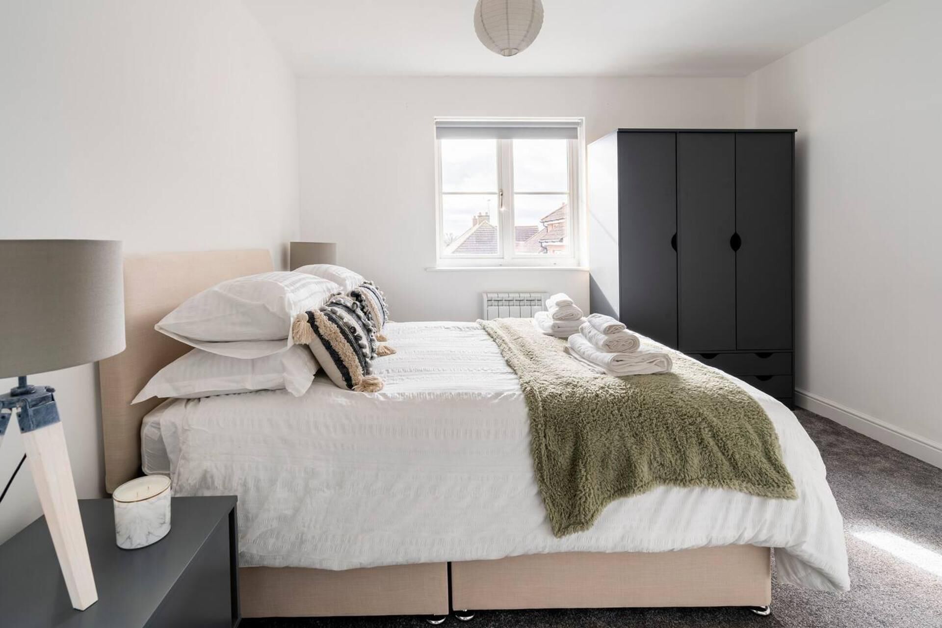 Una camera da letto con un letto, un comodino, una lampada e una finestra che offre vista su edifici.