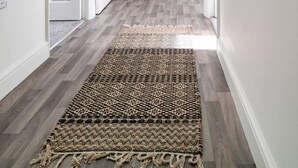 A hallway with a patterned rug, white walls, and a door with a glass panel. - Immaculate 2-bed Apartment in Welwyn Garden City (Welwyn Garden City)