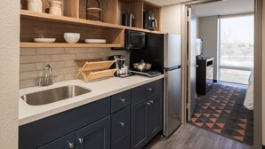 A modern kitchen with a stainless steel sink, black refrigerator, and wooden shelves. - South Country Suites (Mesa)