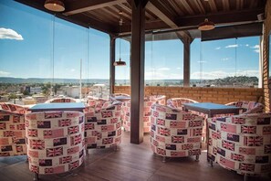 Um bar no terraço com mesas cobertas por bandeiras do Reino Unido, amplas janelas com vista para a cidade e luminárias pendentes.