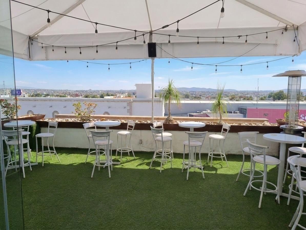 A rooftop terrace with white metal chairs and tables, a white canopy, and a view of the cityscape.