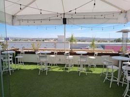 A rooftop terrace with white metal chairs and tables, a white canopy, and a view of the cityscape.